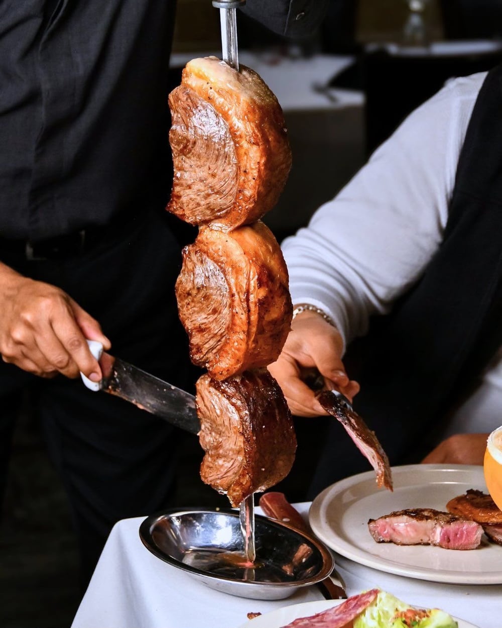 Churrasqueiro fatiando a picanha do espeto na mesa do cliente