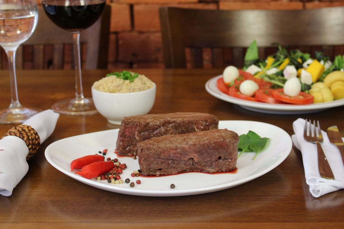 Mesa servida com carne, arroz e salada no salão do Grill Hall