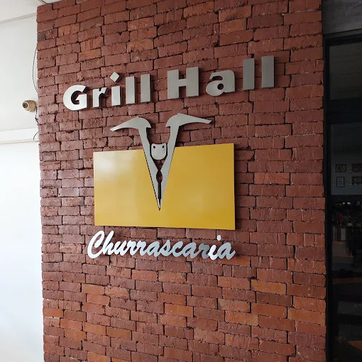 Letras metálicas com o nome Grill Hall Churrascaria aplicadas na parede de tijolo do salão